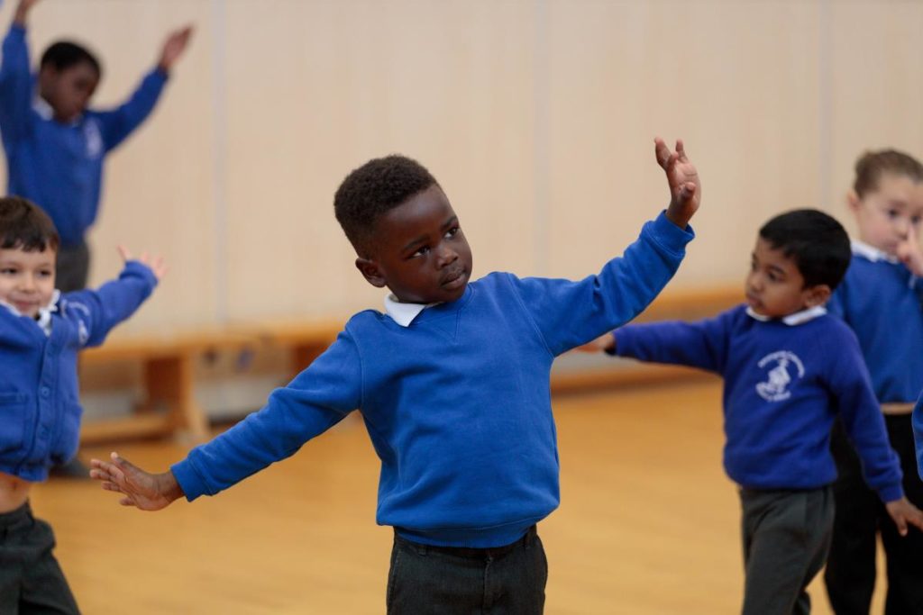 Key stage 1 pupils engaging in drama workshop in their school hall