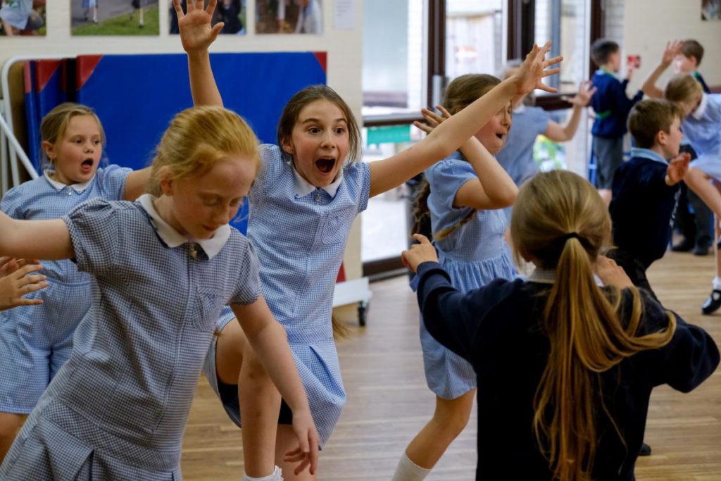 Key stage 2 pupils taking part in a drama workshop in their school hall
