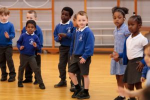 key stage 1 children take part in a drama workshop in their school hall